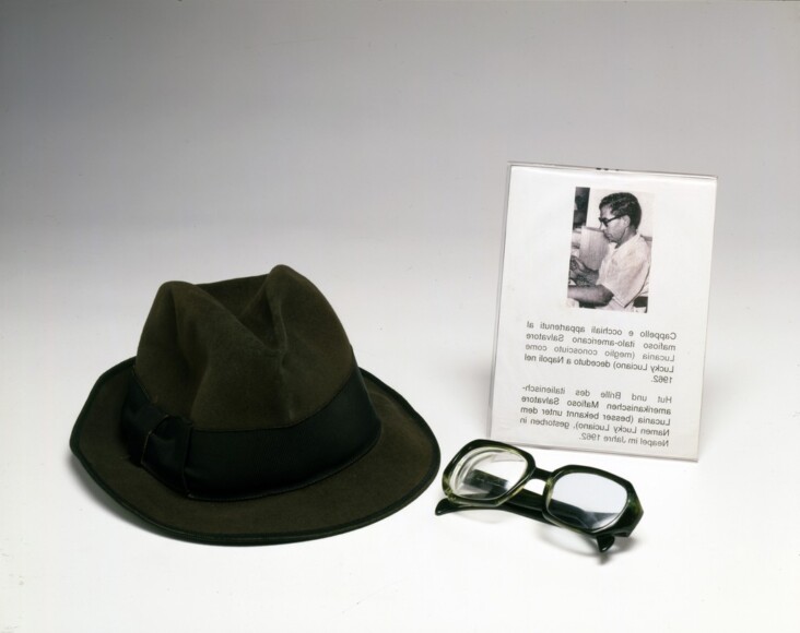 Riello, Antonio , Reliquia di Mafia n. 2 con leggenda di Lucky Luciano, 1993, occhiali, cappello, VAF 1961, Roverto, Mart